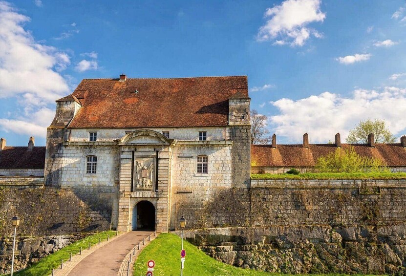 A historic stone building with a central archway, a paved pathway leading to it, and a stone wall in the background. 5