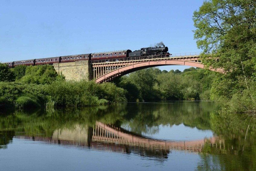 A train crossing a stone bridge over a calm river, surrounded by lush greenery. 3