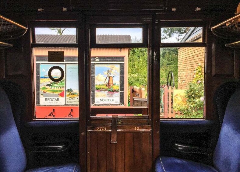 A train interior with wooden paneling, blue seats, and two windows displaying posters of Redcar and Norfolk. 2