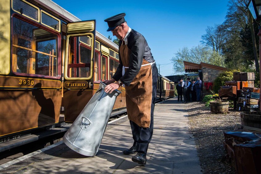 A man in uniform loading a large metal container onto a vintage train. 1