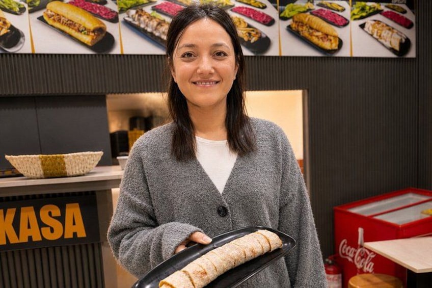 A person holding a tray with food items, standing in front of a counter with a sign that reads 'KASA'. 3