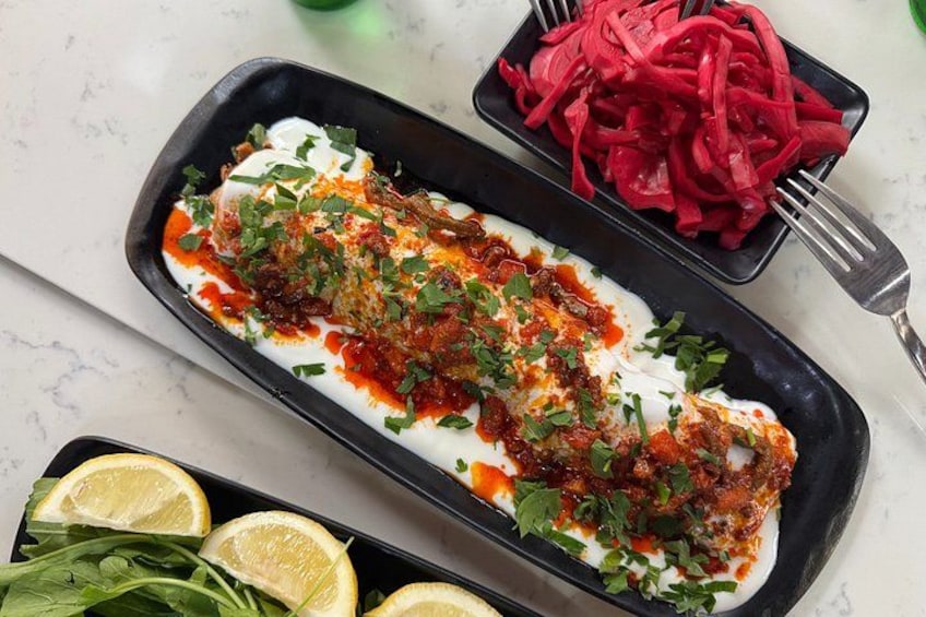 A dish of fish topped with sauce and herbs, accompanied by a side of red vegetables and lemon slices. 1