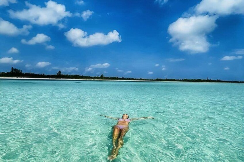A person floating on a clear turquoise sea with a distant shoreline and a clear sky. 5