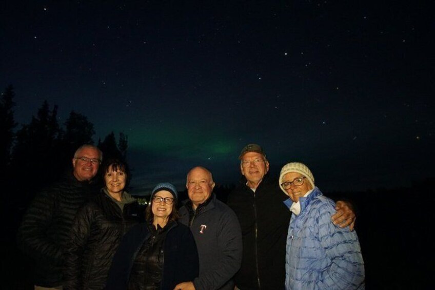 A group of people standing outdoors at night with a starry sky and the aurora borealis in the background. 5