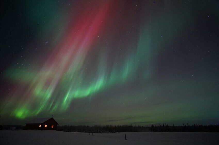 The Northern Lights over a snowy landscape with a small cabin. 4