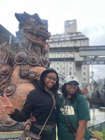 Two people posing in front of a large bronze lion statue with intricate designs. 3