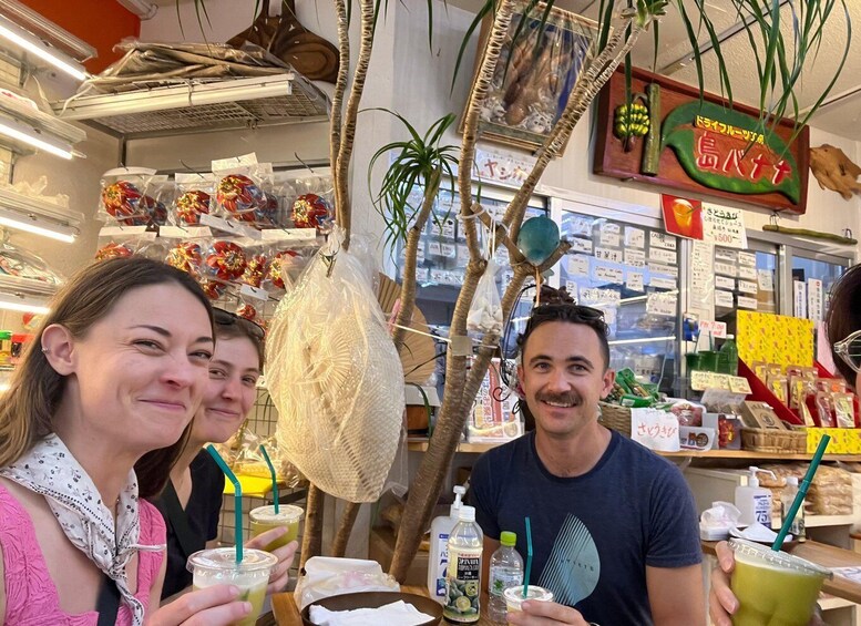 A person holding a drink with a straw, a bottle, and a wrapped item in a store with shelves and a hanging plant. 2