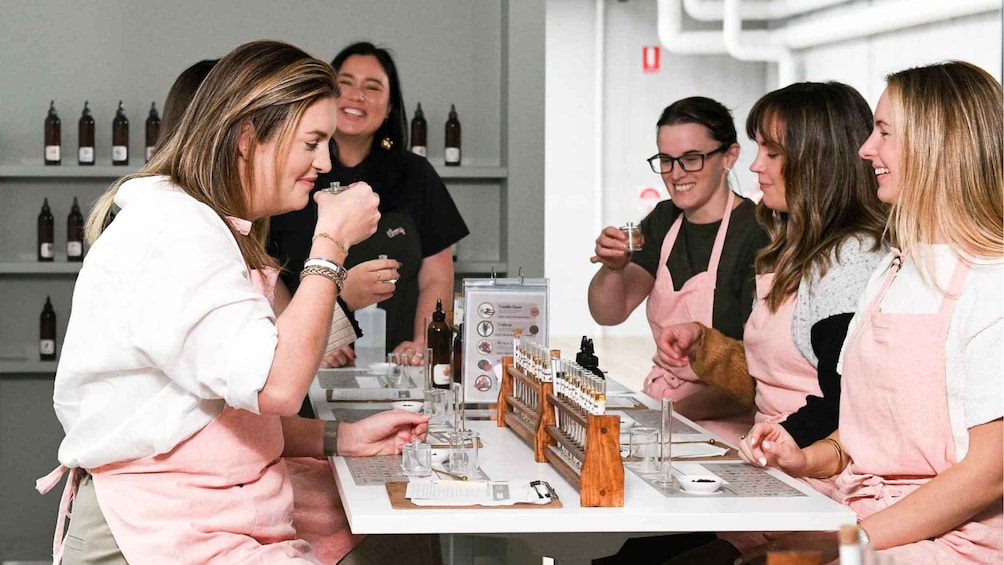 A group of people in aprons at a tasting event with bottles and tasting sheets on the table. 1