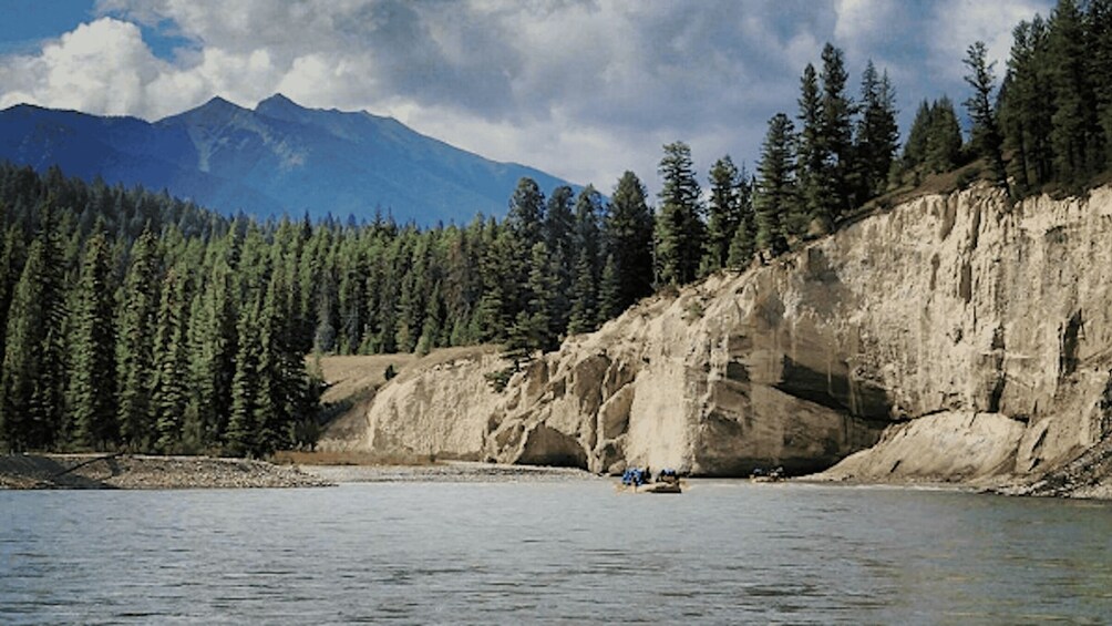 A river with a rocky cliff and a forested mountain range in the background. 2