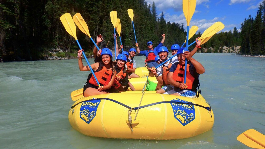 A group of people in a yellow raft on a river, wearing life jackets and helmets, with paddles. 5
