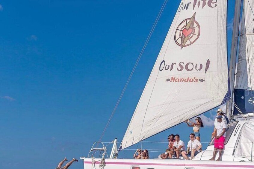 A sailboat with people on deck, a clear blue sky, and a logo on the sail. 2