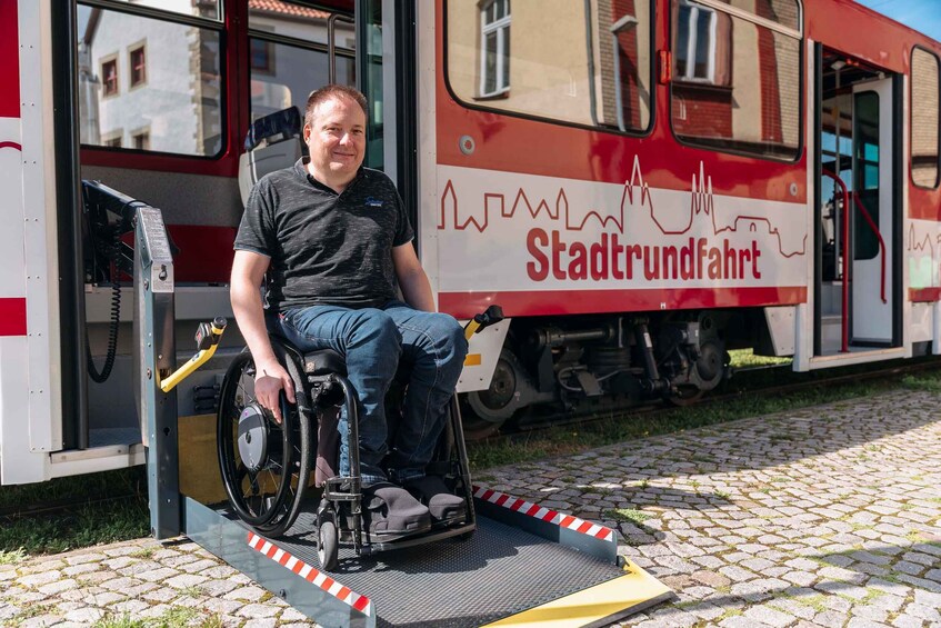 A man in a wheelchair at a train station platform with a red and white train labeled 'Stadtverkehr' in the background. 4