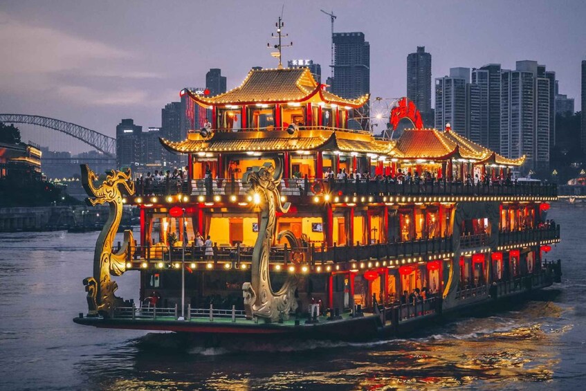 A brightly lit, traditional Chinese boat with ornate decorations, including golden dragons, on a river with a city skyline in the background. 1