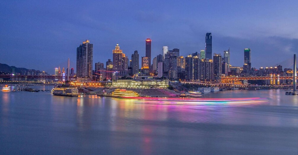 A city skyline at dusk with illuminated buildings and a river with boats. 3
