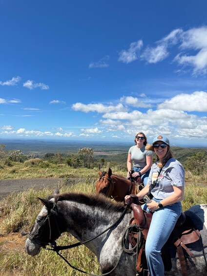 Two people riding horses on a hill with a scenic view of the landscape. 3