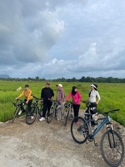 A group of people with bicycles in a field with a cloudy sky. 1