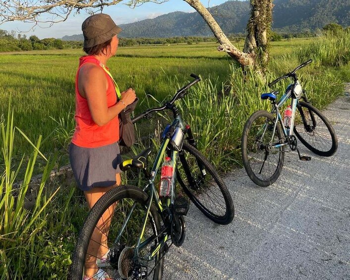 A person standing next to a bicycle on a path with a rural landscape in the background. 2