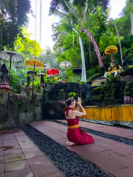 Una persona con un vestido rojo realizando un ritual en un jardín con estatuas y sombrillas. 5