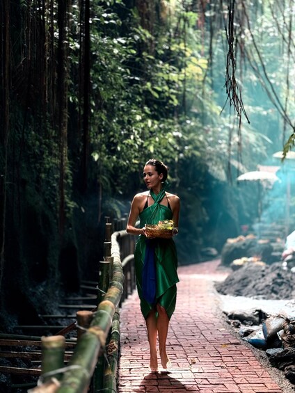 Una mujer con un vestido verde caminando por un sendero de ladrillos a través de una zona boscosa con barandas de bambú. 2