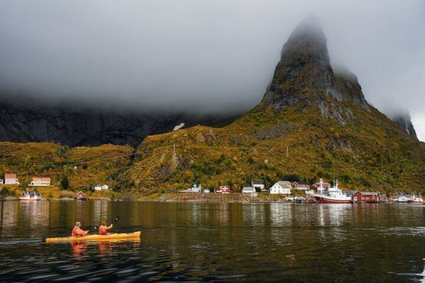 A kayaker on a calm lake with a mountain in the background and a small village. 2