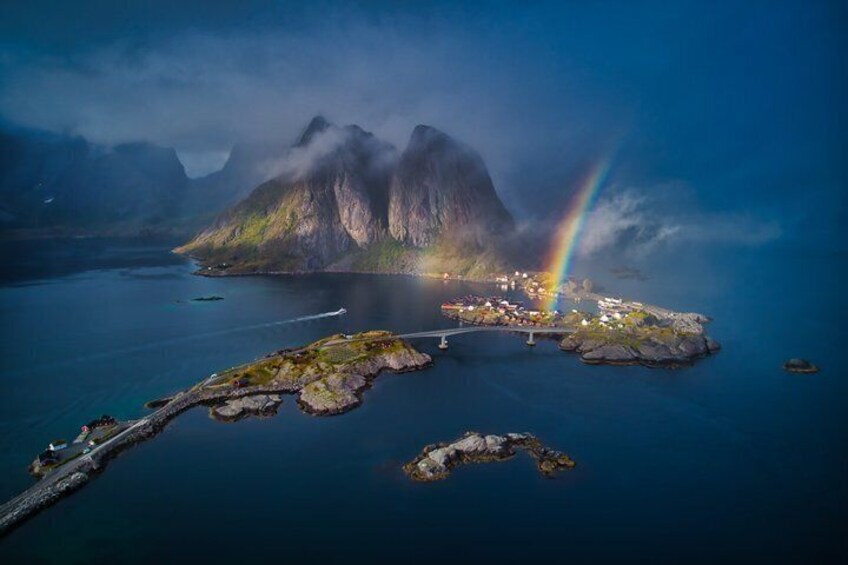A coastal landscape with a mountain, a rainbow, and a small settlement. 1