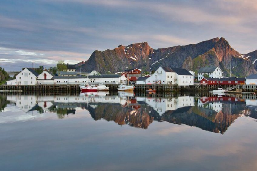 A calm fjord with white buildings and boats, reflecting in the water, and a mountain in the background. 3