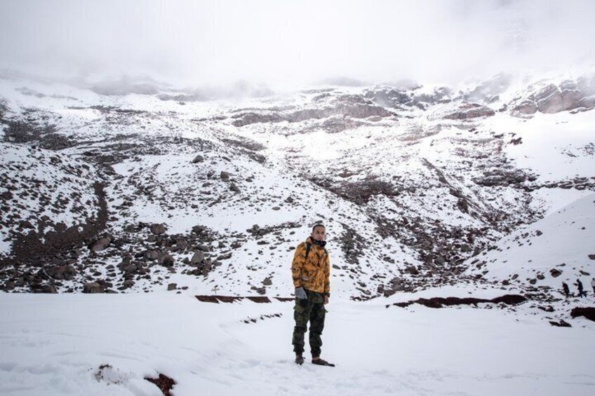 A person standing on a snow-covered mountain with rocky terrain and snow-covered slopes in the background. 3