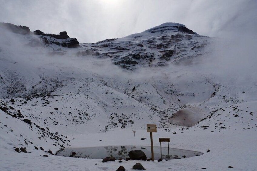 A snow-covered mountain with a small circular structure and two signs in the foreground. 4