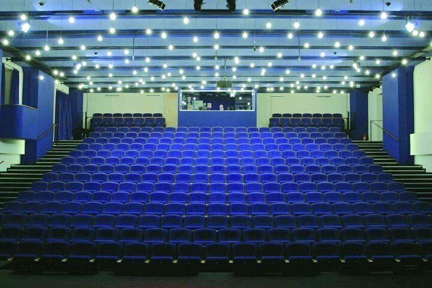 A theater with rows of blue seats, a stage, and a balcony. 3