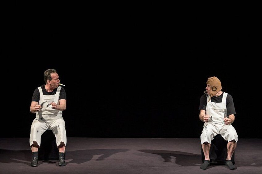 Two individuals seated on stage with a dark background. 2