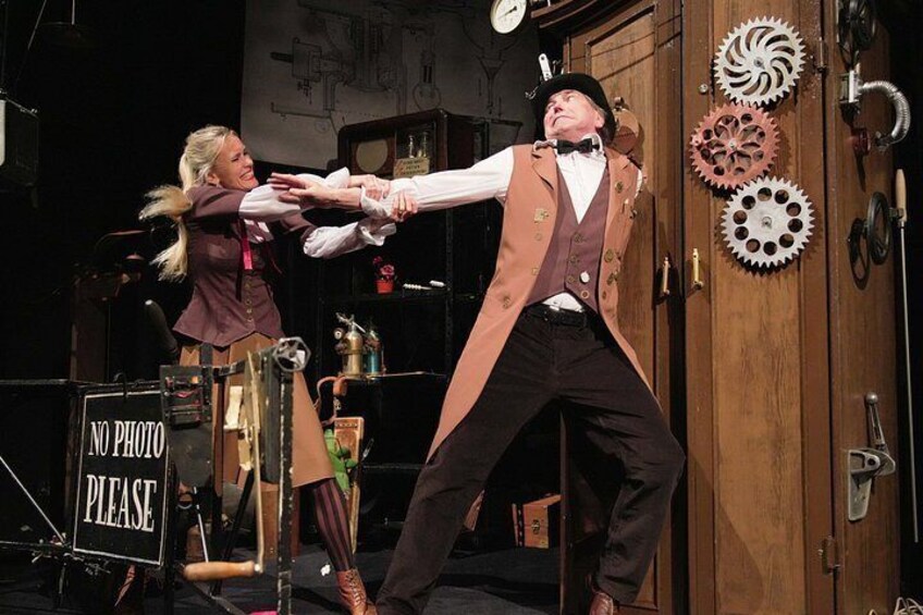 A stage with a 'NO PHOTO' sign, a man in a top hat and vest, and a woman in a dress. 5