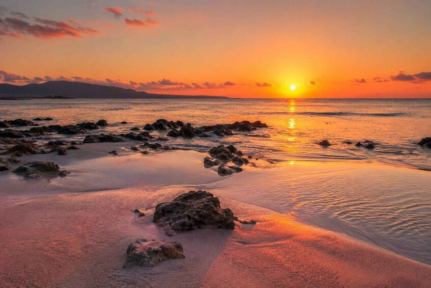 A sunset over a rocky beach with calm waters reflecting the sky. 1