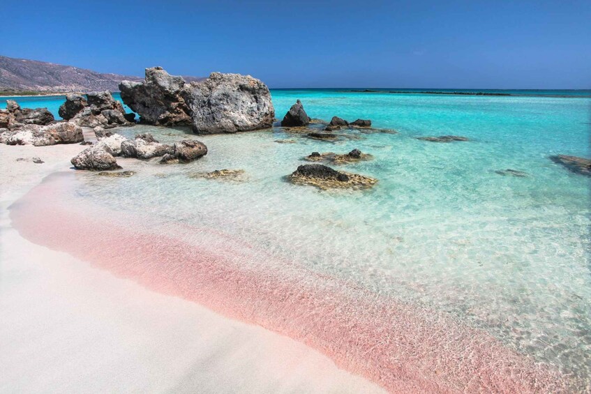 A beach with clear turquoise water, white sand, and scattered rocks. 2