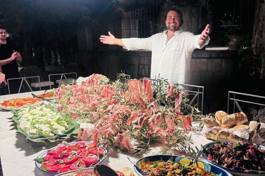 A person standing with arms outstretched in front of a table with various food items. 1