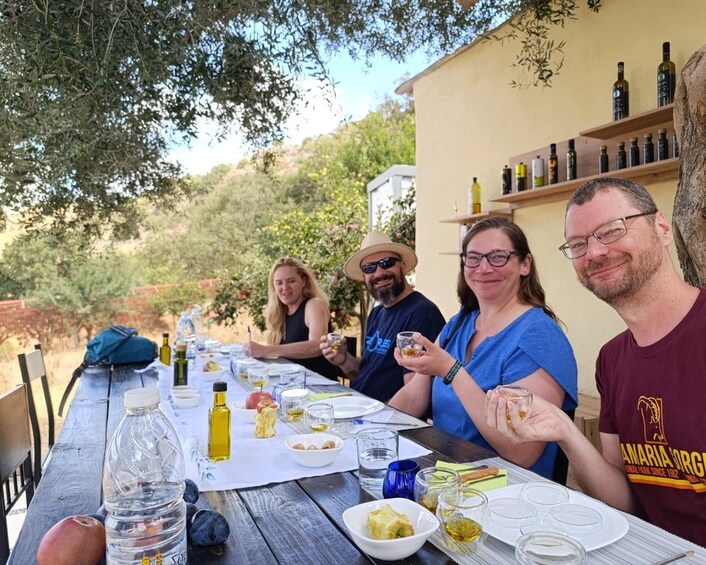 A group of people sitting at an outdoor table with food and drinks, surrounded by trees and a building with wine bottles on display. 5