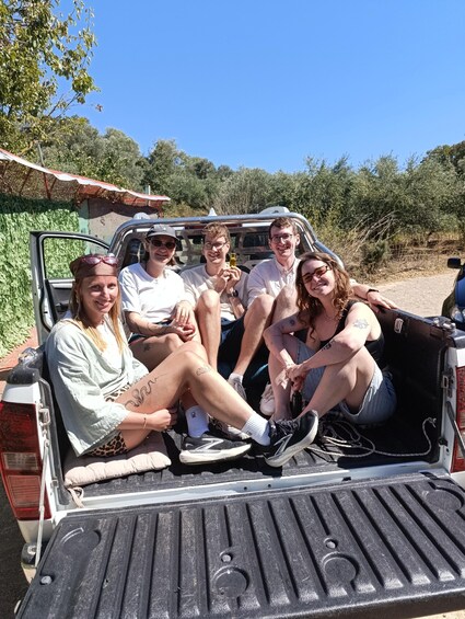 A group of people sitting in the back of a pickup truck with a clear blue sky and greenery in the background. 4
