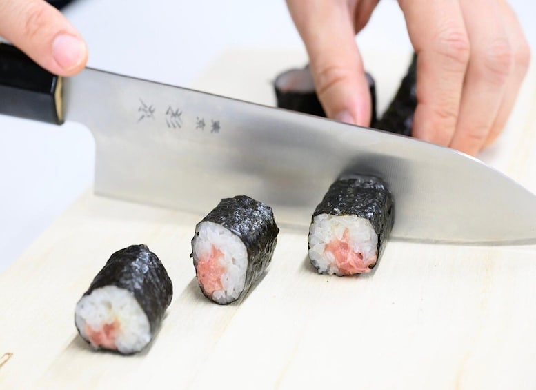 A person cutting sushi with a knife on a cutting board. 4
