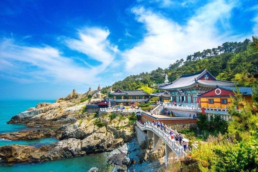 A coastal temple complex with traditional architecture, a stone bridge, and a rocky shoreline. 4