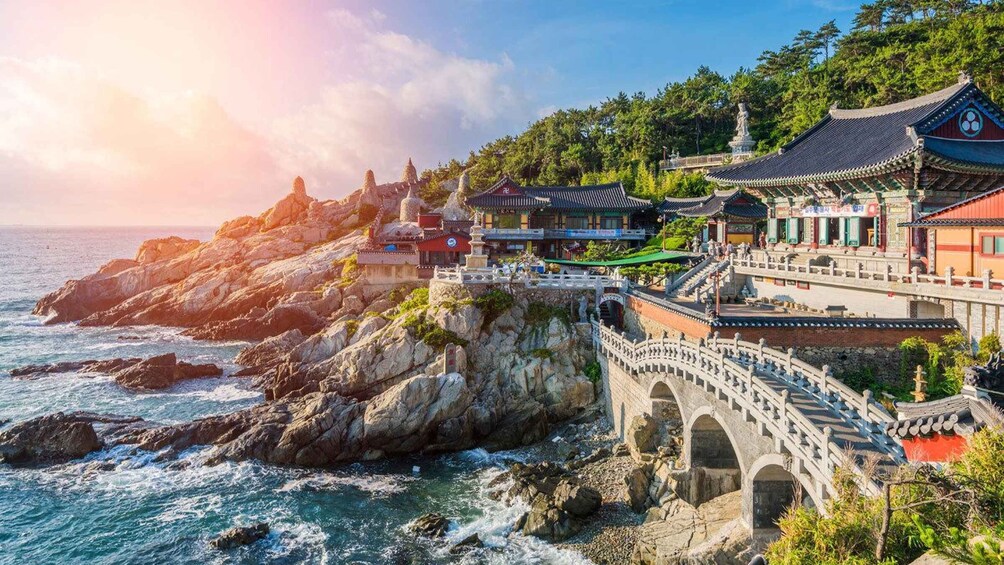 A coastal temple complex with traditional architecture, a stone bridge, and rocky cliffs. 5