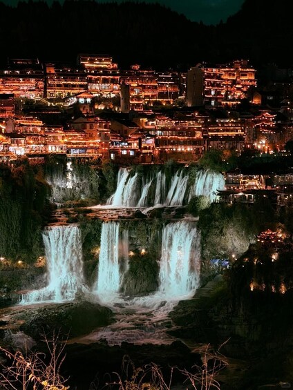 A nighttime view of a traditional village with illuminated buildings and a cascading waterfall. 2