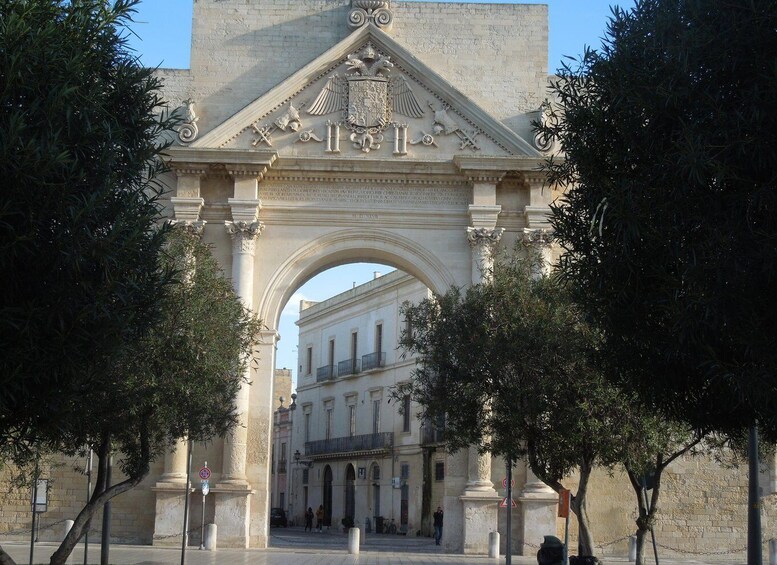 An ornate archway with classical architecture, flanked by trees and leading to a building with multiple windows. 3