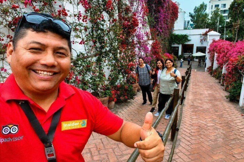 A person in a red shirt giving a thumbs-up gesture, with a brick pathway and flowering plants in the background. 4