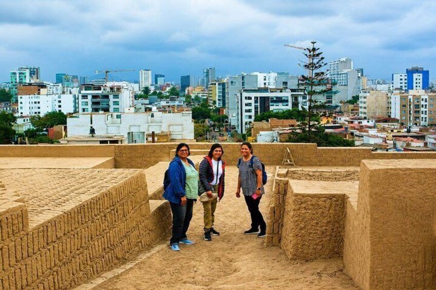 Three people standing in an ancient structure with a cityscape in the background. 2