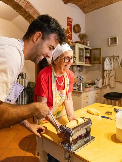 A person using a pasta machine in a kitchen with another individual. 4