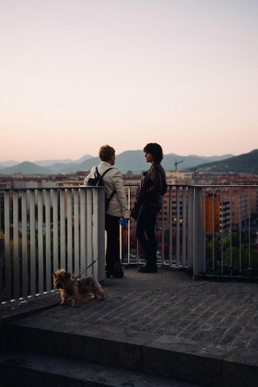 Two people standing on a balcony overlooking a cityscape with mountains in the background. 5