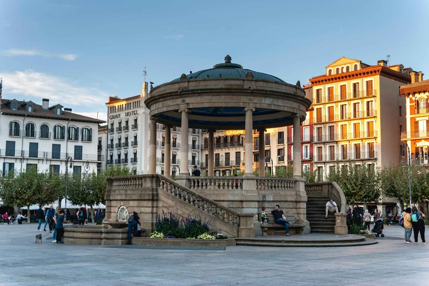 A historic plaza with a central fountain, a round building with columns, and surrounding classical architecture. 3