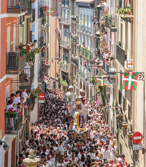 A crowded street with people, balconies, and flags. 1