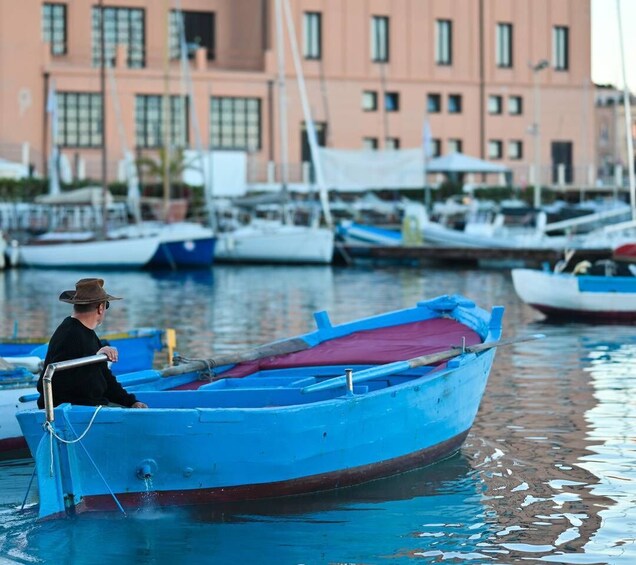 A man in a boat at a marina with buildings in the background. 1