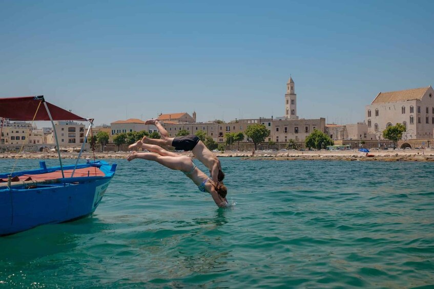 Two people diving into the water from a boat, with buildings and a tower in the background. 3