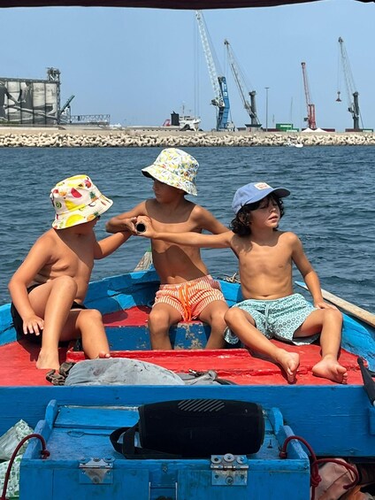 Three children on a boat with a pier and cranes in the background. 2